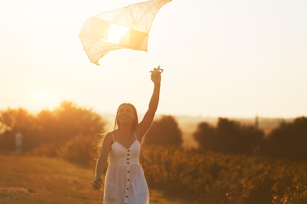 Cheerful woman having fun with kite outdoors on the field at summertime and smiles