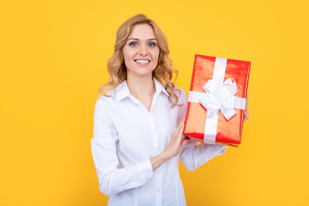 Cheerful woman hold big present box on yellow background