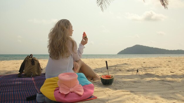 The cheerful woman holding and eating slices of watermelon on tropical sand beach sea