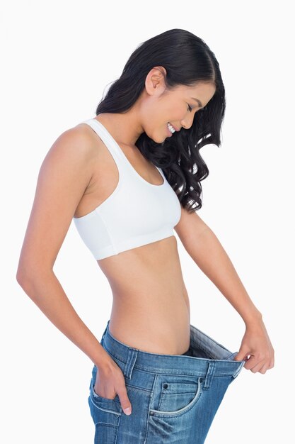 Photo cheerful woman holding her too big jeans