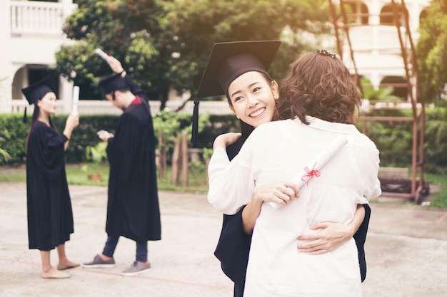 사진 졸업식 의복 을 입은 즐거운 여자 가 야외 에 서 있는 동안 어머니 를 포옹 하고 있다