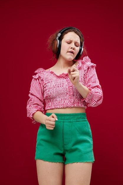 Cheerful woman listening to music with headphones dance on a red background