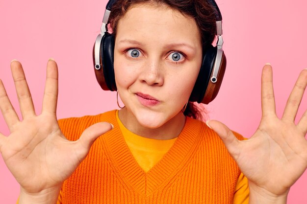 Cheerful woman listening to music with headphones orange sweater emotions fun isolated backgrounds unaltered