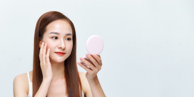 Cheerful woman looking in mirror applying bronzer isolated over white background