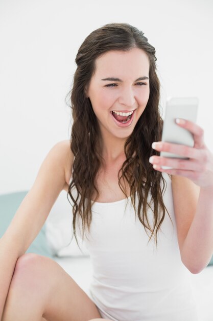 Cheerful woman looking at mobile phone in bed