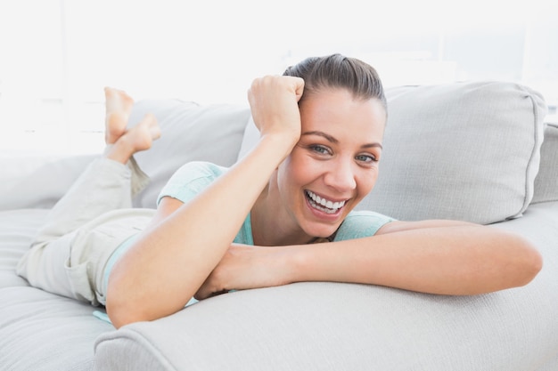 Cheerful woman lying on couch smiling at camera