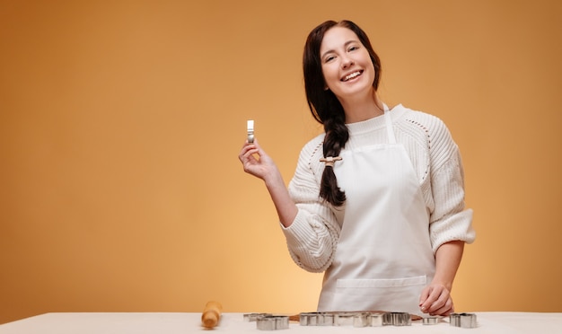 Cheerful woman makes christmas baking homemade cookies using metal molds on a yellow mold