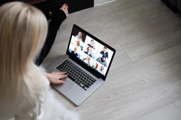 Cheerful woman making video call on Christmas day and greeting somebody, looks happy, clenching fist like winner, looks at screen of device, posing indoor near fireplace