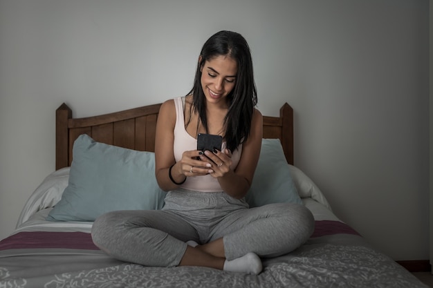 Cheerful woman messaging on smartphone on bed