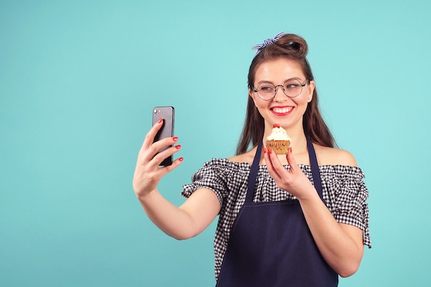 陽気な女性パティシエがカップケーキを手にselfieを作る