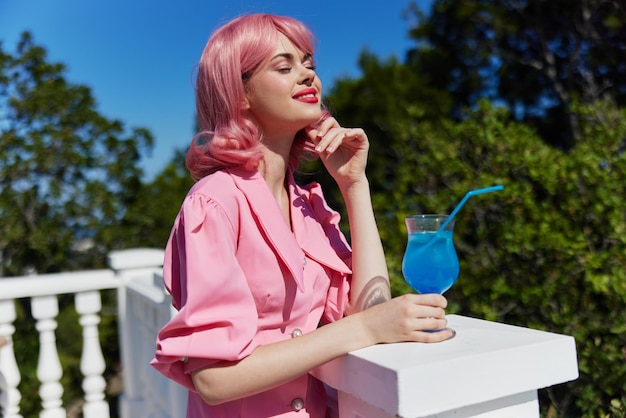 야외에서 칵테일을 마시는 핑크 드레스를 입은 쾌활한 여성 고품질 사진