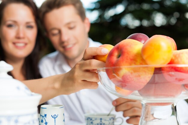 Cheerful woman reaching across the coffee table to a bowl of fruits