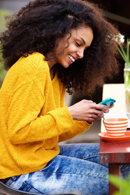 Веселая женщина, читающая текстовое сообщение на мобильном телефоне в кафе