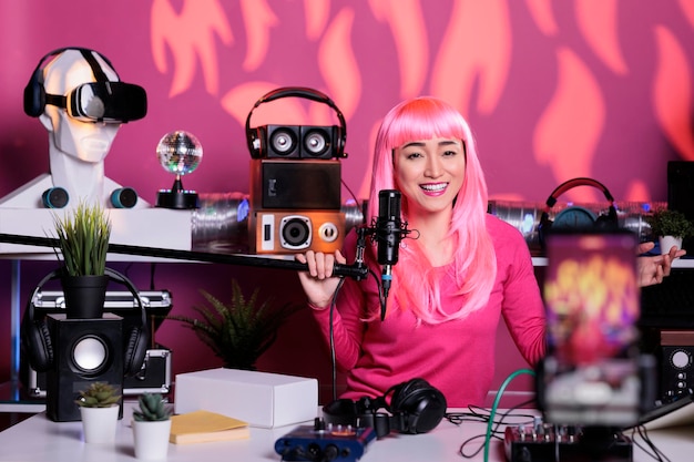 Photo cheerful woman recording podcast using professional streaming equipment while standing in broadcast studio, posting vlog on social media to gain fans. asian creator filming vlog with phone camera