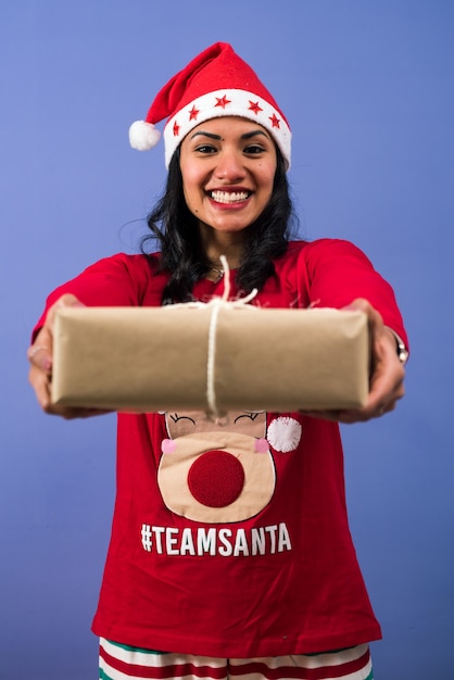 Cheerful woman in a santa hat giving a Christmas present