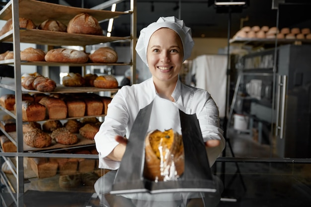 Photo cheerful woman seller giving fresh loaf of bread in packet