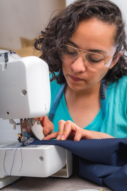 Cheerful woman sewing while sitting at her working place in fashion workshop