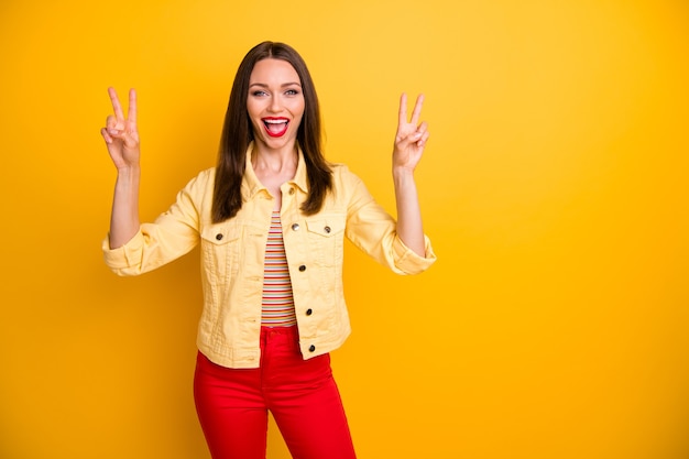 cheerful  woman showing double v-sign in trousers with mouth open isolated vivid color wall