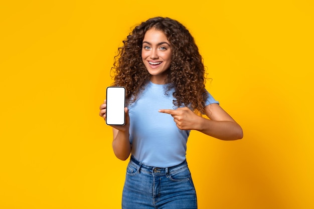 Cheerful woman showing smartphone screen on yellow