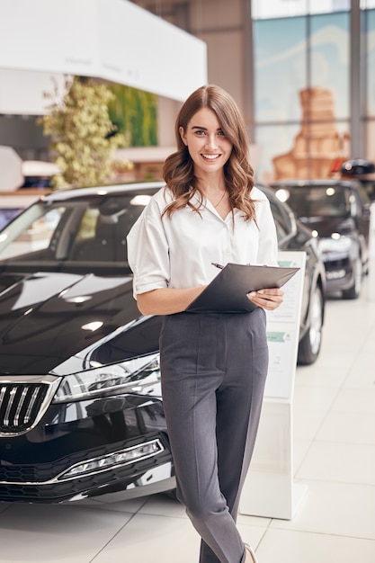 Cheerful woman signing papers in car salon