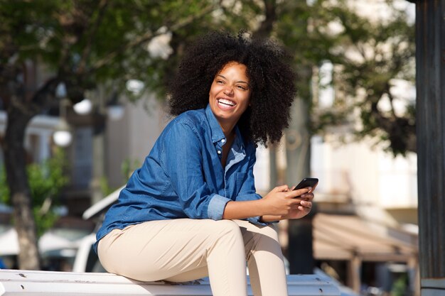 Cheerful woman sitting outside with mobile phone