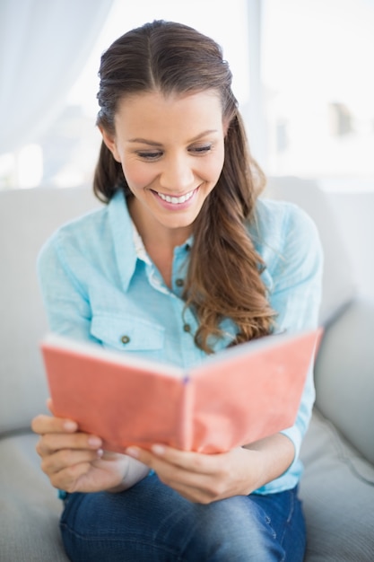 Cheerful woman sitting on sofa reading book