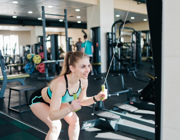 Cheerful woman in sportswear does exercise in the skier's simulation machine in the gym.