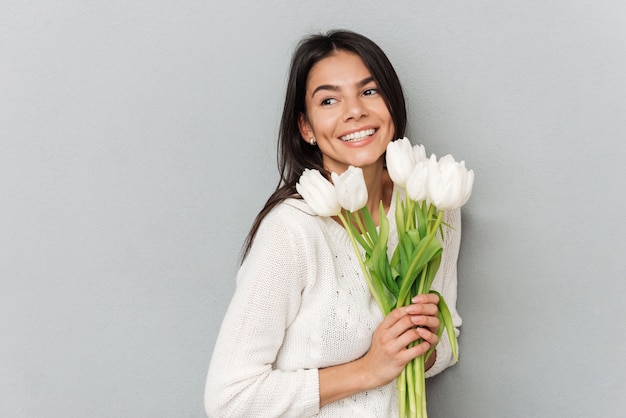 Cheerful woman standing over grey wall with flowers