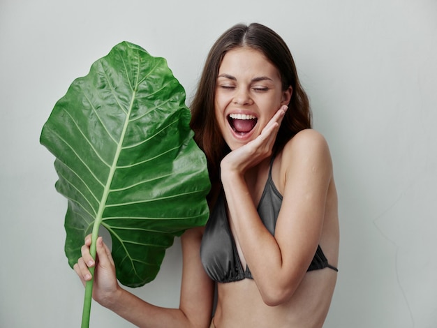 Cheerful woman in swimsuit palm leaf holding the charm of the tropics