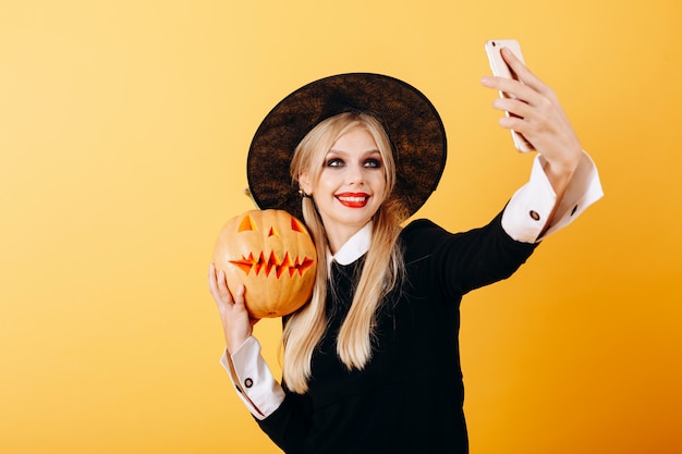 Cheerful woman take a selfie picture portrait against a yellow   holding pumpkin 