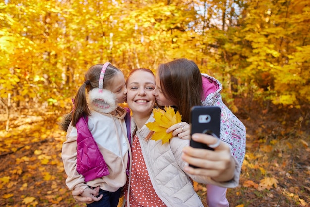 A cheerful woman takes selfies with her daughters in an autumn park family photos of happy people