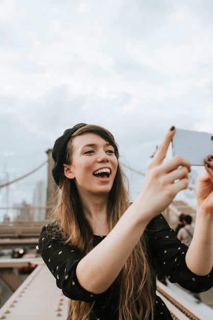 Photo cheerful woman taking a selfie with the brooklyn bridge, usa