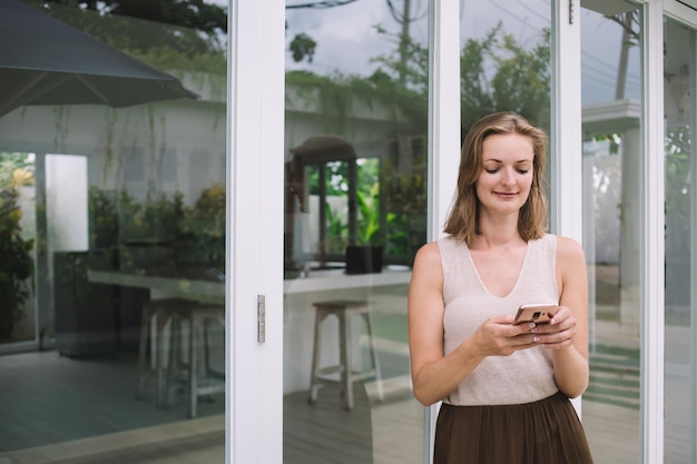 Cheerful woman typing on cellphone in villa yard