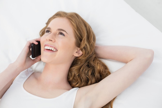 Cheerful woman using mobile phone in bed