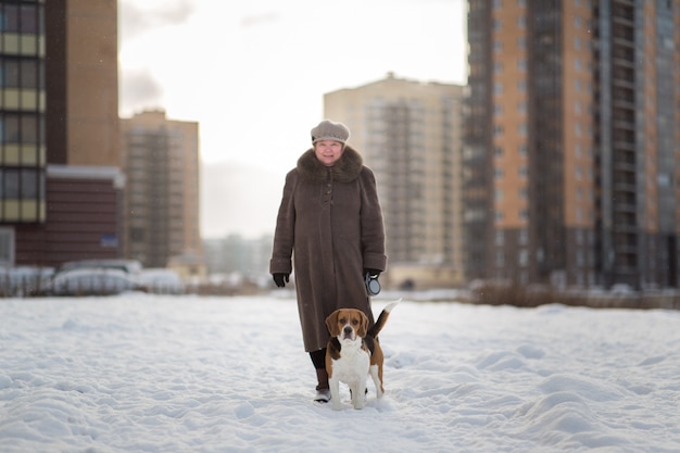 Cheerful woman walking with a dog on a meadow in winter