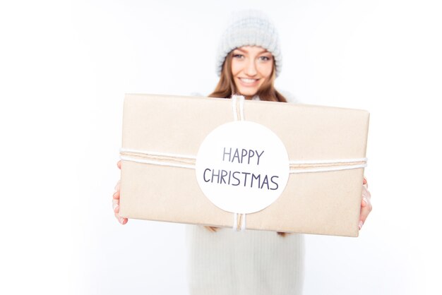 Cheerful woman  in warm hat and scarf holding package and congratulate with xmas