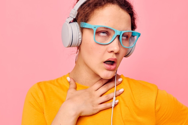 Cheerful woman wearing blue glasses listening to music on headphones isolated backgrounds unaltered