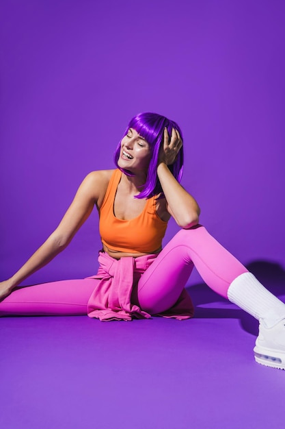 Photo cheerful woman wearing colorful sportswear sitting against purple background