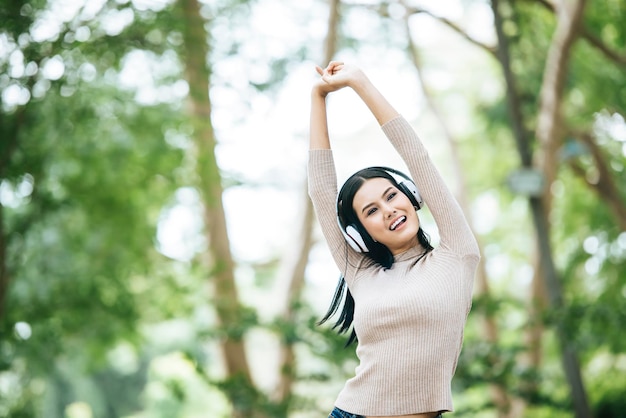 写真 樹木に寄りかかって立っているときヘッドフォンをかぶった陽気な女性