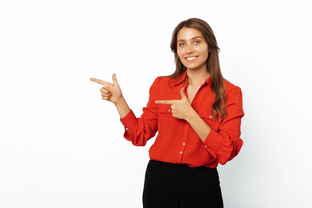 Cheerful woman wearing red shirt points aside to copy space with two fingers
