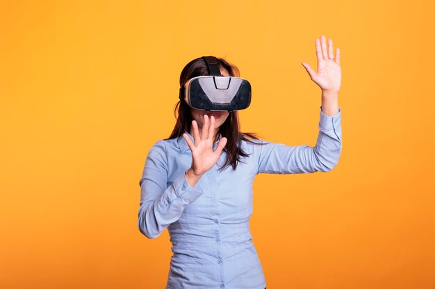 Cheerful woman wearing vr goggles enjoying 3d simultation in studio over yellow background, enjoying digital entertainment. electronic futuristic experience with augmented tech innovation