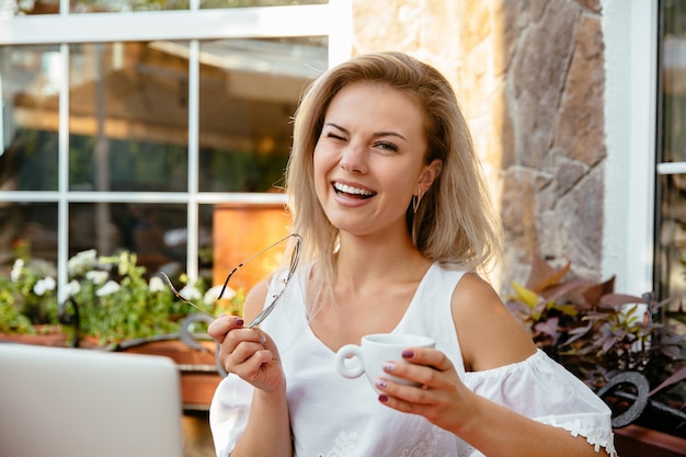 Cheerful woman winking while holding a cup of coffee, resting at the cafe