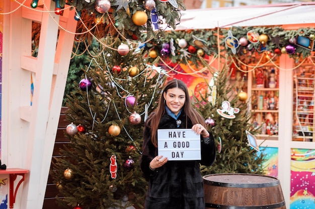 Cheerful woman wishing a good day using tablet, girl outdoors at Christmas fair in winter.