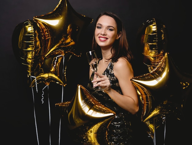 Cheerful woman with balloons laughing on black background.