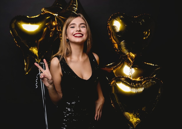 Cheerful woman with balloons laughing on black background.