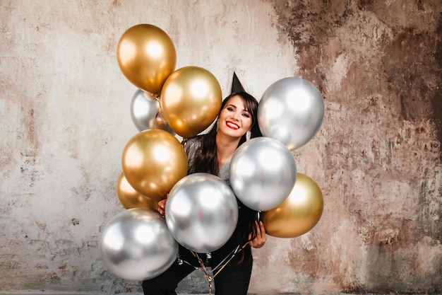 A cheerful woman with balloons laughs a young brunette with long hair celebrates her birthday helium balloons