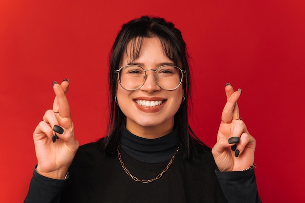 Cheerful woman with black hair is crossing fingers while wishing for something