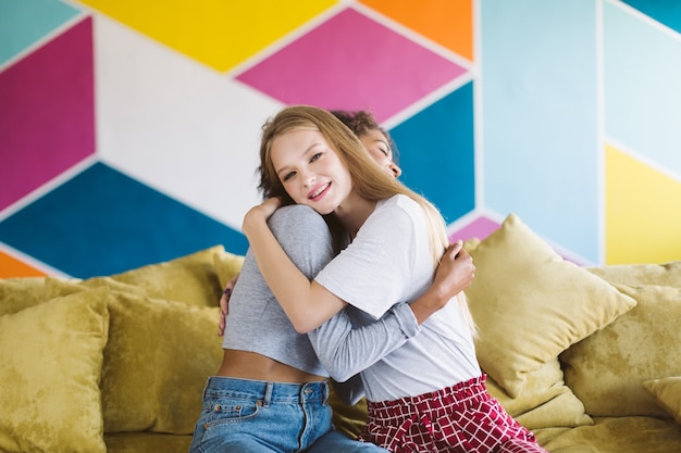 Cheerful woman with blond hair hugging girlfriend while happily  with colorful wall 