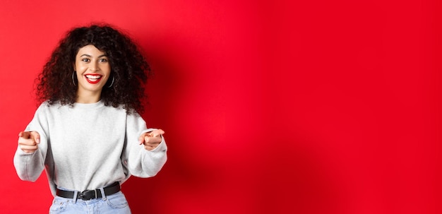 Cheerful woman with curly hair inviting you recruiting newbies pointing fingers at camera and smilin