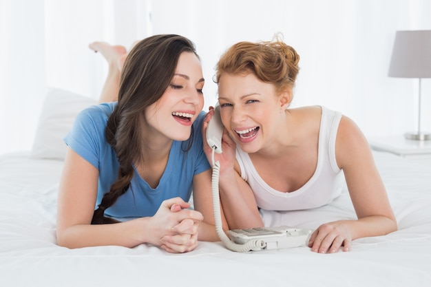 Cheerful woman with friend using phone in bed